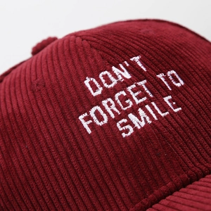 Macro detail of wine red corduroy fabric texture and white letter embroidery on baseball cap