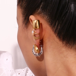 Close-up of stacked gold ear cuffs and pearl hoops on a female model's ear