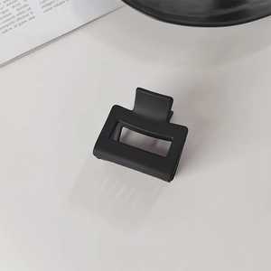 Gros plan d'une pince à cheveux rectangulaire noire mate sur une surface blanche