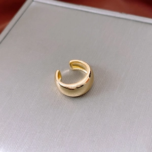 Nahaufnahme einer minimalistischen vergoldeten Ohrmanschette für Ohren ohne Ohrlöcher auf Grau