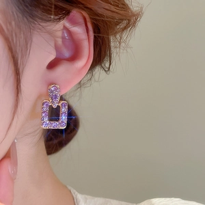 Primo piano dell'orecchino a perno quadrato dorato con strass viola indossato dal modello