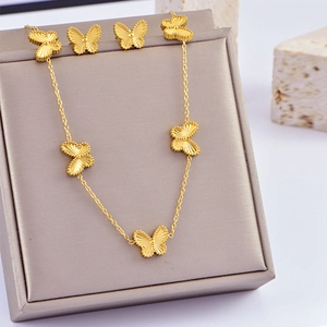 Detailed close-up of golden butterfly necklace and earrings set on a grey display stand