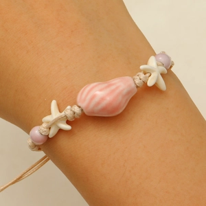 Detail of hand-woven bracelet with pink shell bead and white starfish on person wrist