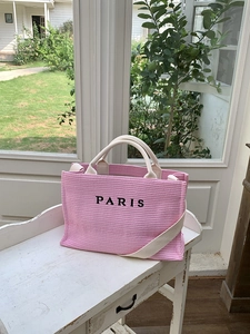 Detailed texture of pink woven tote bag with black PARIS embroidery on a wooden table