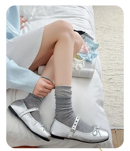 Detail of silver Mary Jane shoes paired with grey slouch socks on a white fabric surface