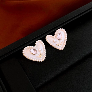 Macro shot of heart earring with white enamel tulip pattern and golden pearl border