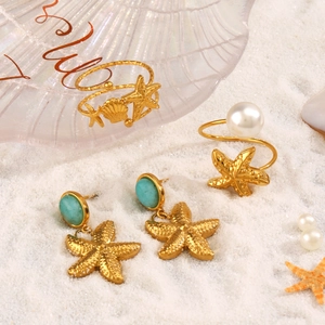 Set gioielli dorati con stelle marine e conchiglie su sabbia bianca per stile spiaggia