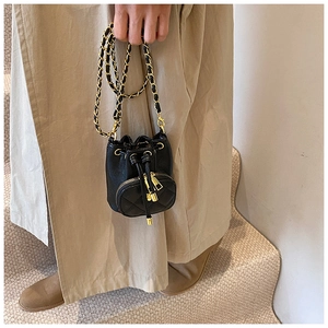 Detail of a mini black quilted bucket bag with gold chain strap held by a model