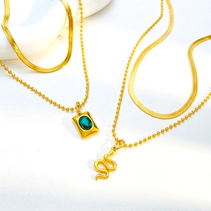 Detail of layered gold necklaces with emerald pendant, snake charm, and flat snake chain