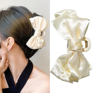 Detail of a cream satin bow hair claw clip showing both model wear and material texture