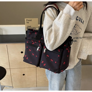 Detail of printed tote bag with cherry pattern and multiple pockets worn by a model