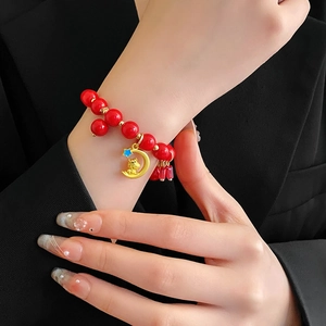 Détail d'un bracelet de perles rouges avec charms dorés sur un fond en tissu noir