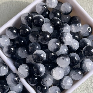 Macro detail of 10mm black and white ice-cracked glass beads in a white tray for DIY crafts