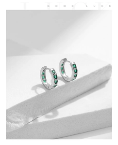 Detail of silver S925 earrings with green heart-shaped zirconia on a white stone base