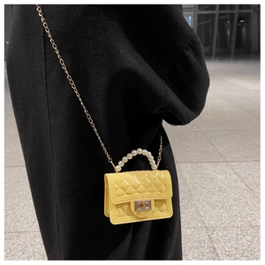 Detail of yellow quilted silicone mini bag with pearl handle and golden chain strap
