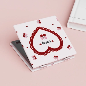 Close-up of portable square cherry makeup mirror with red heart patterns on pink background