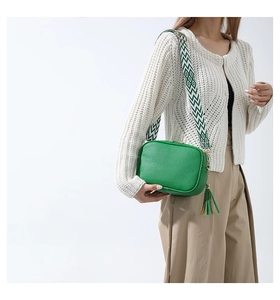 Borsa camera verde in pelle con ampia tracolla geometrica e nappina indossata dal modello