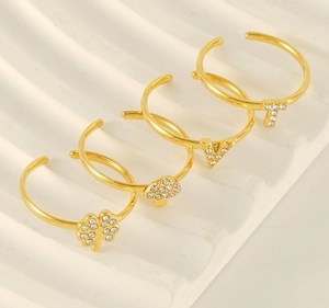 Detail of four gold adjustable rings with clover, mushroom, and letter charms on a tray