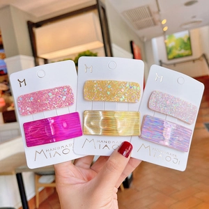 Three sets of holographic laser glitter hair clips for girls shown in hand on cards