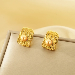 Close-up of gold irregular wrinkled rectangular earrings with pearl inlay on soft fabric