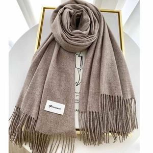 Detail of dark khaki cashmere scarf with long tassels displayed on a gold frame