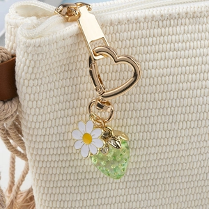 Detail of strawberry charm with daisy pendant and gold heart clasp on woven bag