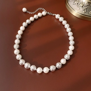 Detailed shot of white pearls and frosted silver beads on a brown textured surface