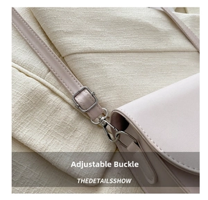 Close-up of bright silver metal adjustment buckle and stitching on beige leather saddle bag