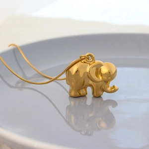 Polished gold elephant pendant necklace with snake chain for men and women on ceramic tray