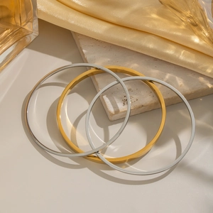 Drei minimalistische geometrische Armreifen in Gold und Silber auf Marmoroberfläche