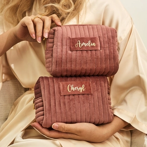 Detail view of two personalized pink velvet makeup bags with gold zippers and custom names