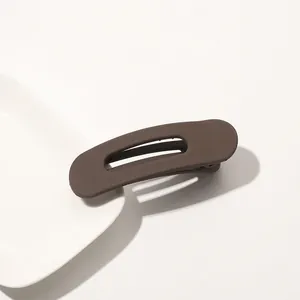 Detail view of the matte dark brown oval cutout hair clip on a minimalist white plate