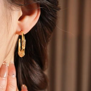 Primo piano di orecchini a cerchio ritorti a forma di C placcati in oro 18K con zirconi