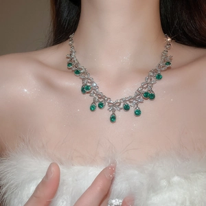 Close-up of elegant silver necklace with green water-drop and round gemstones on neck