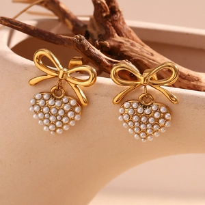Macro shot of gold bow heart earrings with white pearls on a textured background