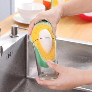 Avocado shaped multi-layer cleaning sponge scrubbing a glass cup in a bright kitchen