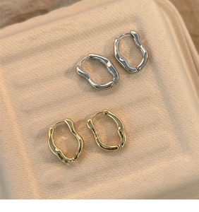 Macro view of gold and silver irregular wavy hoop earrings with lava texture on beige fabric