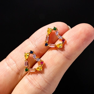 Golden heart-shaped stud earrings with colorful zircon stones held against a dark background