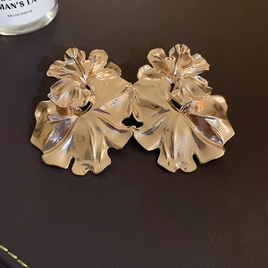 Detailed view of large gold floral earrings with textured petals on leather surface