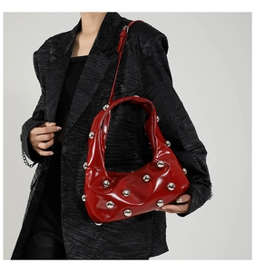 Detail view of red patent leather shoulder bag featuring silver metal spherical rivets