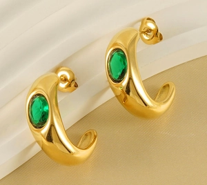 Close-up of gold-plated C-shaped earrings with oval green zircon inlay on textured base