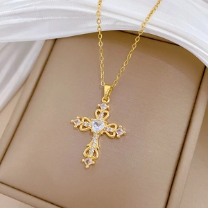 Macro shot of gold cross necklace with hollow heart and square crystals on silk
