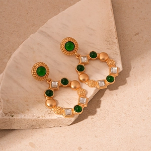 Detailed close-up of vintage gold circular earrings with green resin and square crystals