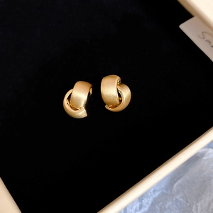 Detail of matte gold brushed C-shape knot stud earrings on black velvet background