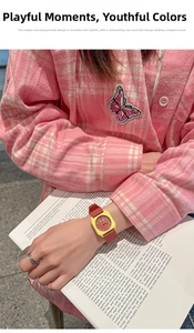 Detail of red and yellow silicone watch worn against a pink checkered jacket and book