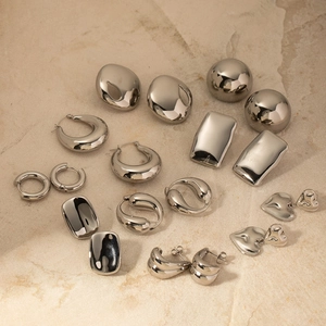 Polished silver stainless steel earrings in various geometric shapes on beige stone