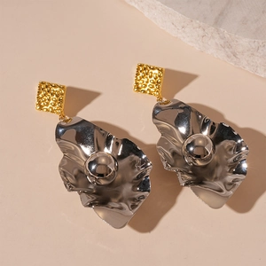 Detail of gold textured square and silver irregular liquid metal earrings on beige stone