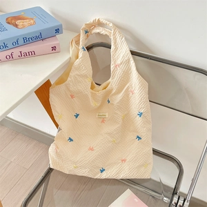 Detail of waffle-textured beige tote bag with colorful embroidered bows on transparent chair