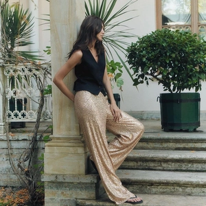 Detail shot of shimmering gold sequin wide-leg trousers and black vest on a model