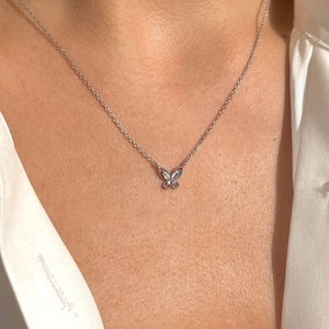 Detail of silver butterfly necklace with opal wings worn on the collarbone of a model